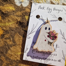 Load image into Gallery viewer, A close up view of the ghost necklace showing the detail in the bunch of flowers. The necklace has a silver chain and sits on a white backing card with the words ‘Duck Egg Designs’ in black handwriting. Behind the backing card you can see a warm brown retro floral patterned fabric. 
