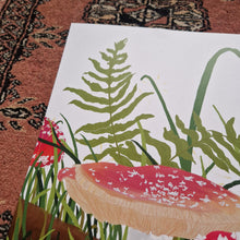 Load image into Gallery viewer, A close up of the top left of the print showing the top of the main fly agaric fungi as well as the green grasses and ferns on the white background. Above and to the left of the print you can see a red textured patterned background. 
