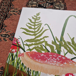 A close up of the top left of the print showing the top of the main fly agaric fungi as well as the green grasses and ferns on the white background. Above and to the left of the print you can see a red textured patterned background. 