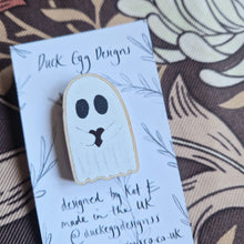 Load image into Gallery viewer, A close up of a wooden ghost pin featuring a ghost holding a red heart. The pin sits on a white and black backing card in front of a brown retro floral background.
