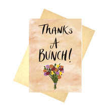 Load image into Gallery viewer, An orange abstract background card sits on a brown envelope in front of a white background. The card features a bunch of flowers in orange, pink, yellow and red below the words ‘Thanks An BUNCH!’ In black handwriting.
