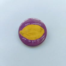 Load image into Gallery viewer, A pink badge sits on a white background. The badge features a yellow textured lemon with the words &#39;when life gives you lemons MAKE LEMONADE&#39; in white.
