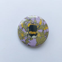 Load image into Gallery viewer, A lilac circle badge sits on a white background. The badge features a fluffy yellow black and white bumble bee, with a honeysuckle plant behind it.
