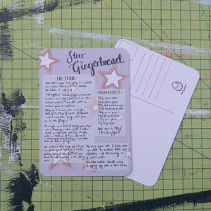 Front and back of a postcard are visible on a green cutting mat. The front is pale purple with a handwritten star gingerbread recipe. The back is white with lines for the address and a square for the stamp as well as the duck egg designs logo.