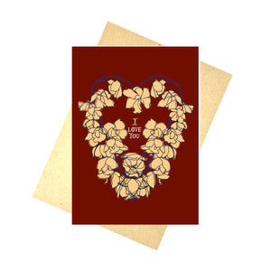 A rich red card featuring a heart made with  yellow orchids. In the middle of the heart are the words 'I LOVE YOU' in white. Behind the card is a brown envelope behind which is a white background.