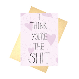Muted pink card with hearts all over it and the words 'I THINK YOU'RE THE SHIT' in black across it. Behind the card is a brown envelope, behind which is a white background.