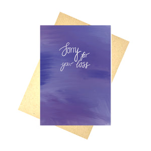 Blue textured card featuring the words 'Sorry for your loss' in white calligraphy. Behind the card is a recycled brown envelope, behind which is a white background.
