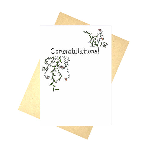 A white card with the word 'Congratulations!' in black handwriting. On the bottom left and top right of the word there are green leafy vines and flowers. Behind the card is a recycled brown paper envelope behind which is a white background.
