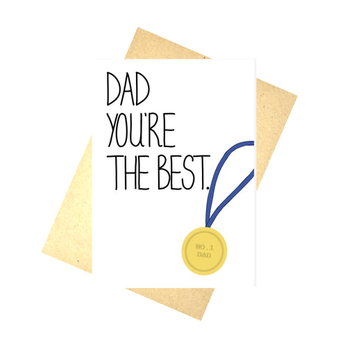 A white card on top of a brown envelope and a white background. The card features the words DAD YOU'RE THE BEST along the left hand side in black handwriting. On the right angled towards the middle of the card is a golden medal that reads NO. 1 DAD with a blue ribbon falling off the side of the card.