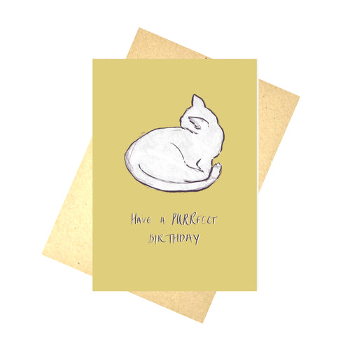 A rich yellow card with a white cat sits on top of a brown envelope in front of a white background. The card reads 'HAVE A PURRFECT BIRTHDAY' in purple and white handwriting. The cat also has a purple outline.
