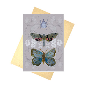 A grey-pink card featuring a layered design created using illustrations from my sketchbook. Central to the card are a rhino beetle, a tropical moth and a blue butterfly. Behind the card is a brown envelope, behind which is a white background.