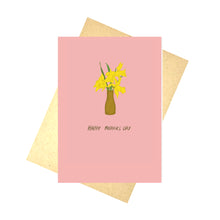Load image into Gallery viewer, A warm pink card featuring a brown vase filled with yellow daffodils sits above the words &#39;Happy Mothers Day&#39;. Behind the card is a brown envelope, which is in front of a white background.
