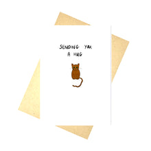 Load image into Gallery viewer, White card featuring a small brown cat with green eyes. Above the cat are the words &#39;SENDING YOU A HUG&#39; in block handwriting. Underneath the card is a brown envelope in front of a white background.
