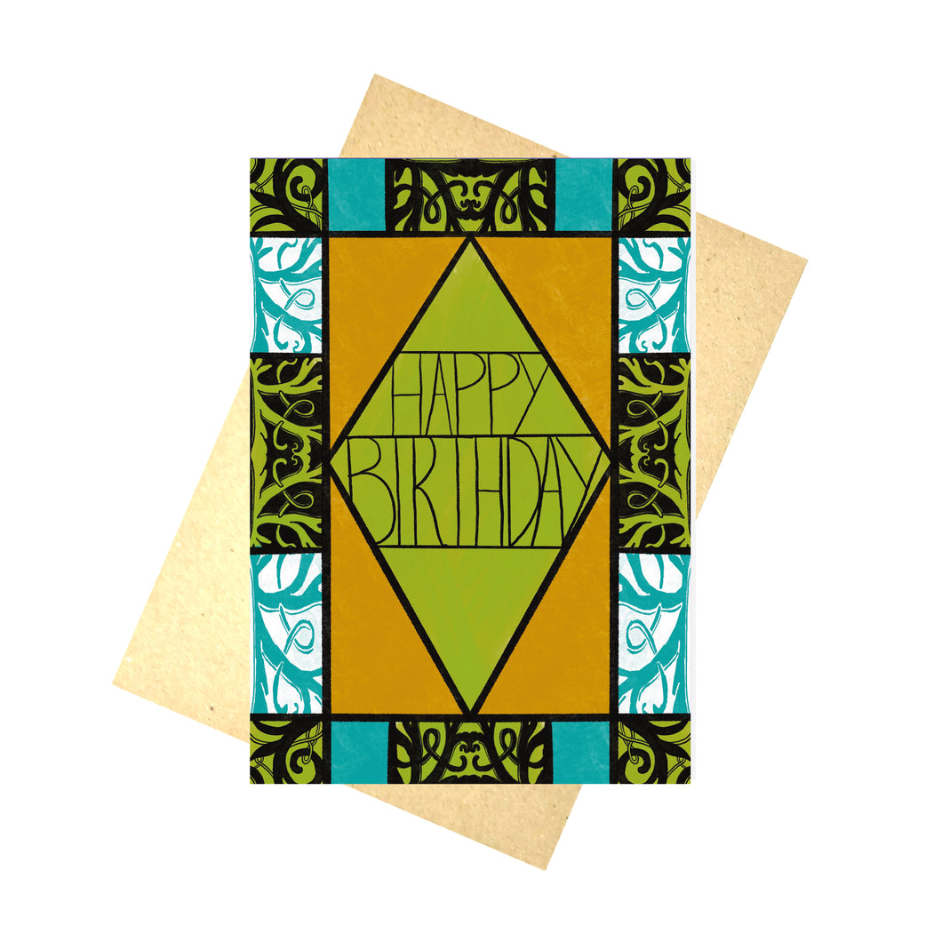 A colourful card sits in front of a brown envelope on a white background. The card featured the words 'HAPPY BIRTHDAY' in the middle in black writing in front of a green background in a black outlines diamond. Around the green filled diamond is a vertical rectangle filled with a warm orange. Around the border of the card is different sections of patterned and unpatterned boxes in green, black, blue and white.