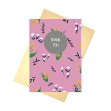 Load image into Gallery viewer, Pink card featuring dark green leafy vines, white fluffy flowers and mustard yellow tulips in an all over pattern. Central, towards the top of the card is a grey circle, with the words THANK YOU written in white. Behind the card is a brown envelope, behind which is a white background.
