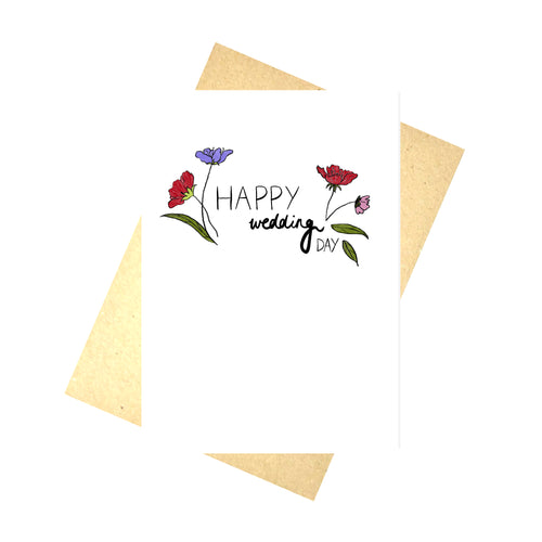 A white card featuring the words 'HAPPY wedding DAY' in black handwriting. To the left and right of the cards you can see red, purple and pink flowers growing from the words with some green leaves. Behind the card you can see a recycled brown envelope behind which is a white background.